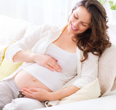 Pregnant Happy smiling Woman sitting on a sofa and caressing her