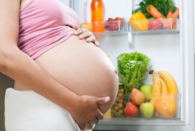 pregnant woman and refrigerator with health food vegetables and