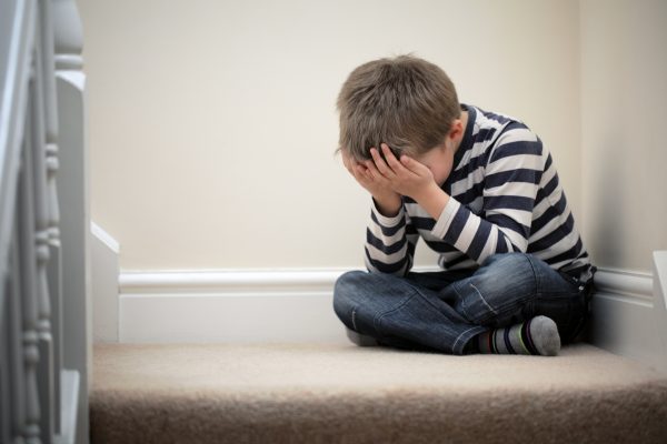 Upset problem child with head in hands sitting on staircase conc